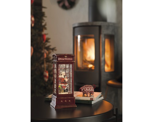Boule à neige décorative en forme de cabine téléphonique avec motif de Père Noël et cheminée en arrière-plan.