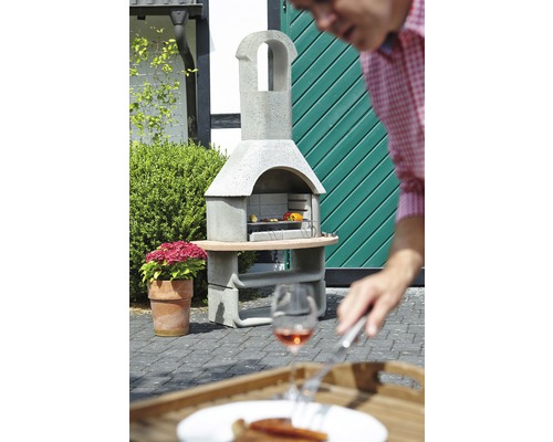 Barbecue en pierre avec nourriture dans le jardin et une personne au premier plan