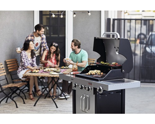 Des personnes font des grillades sur une terrasse avec un barbecue à gaz et savourent un repas à table.