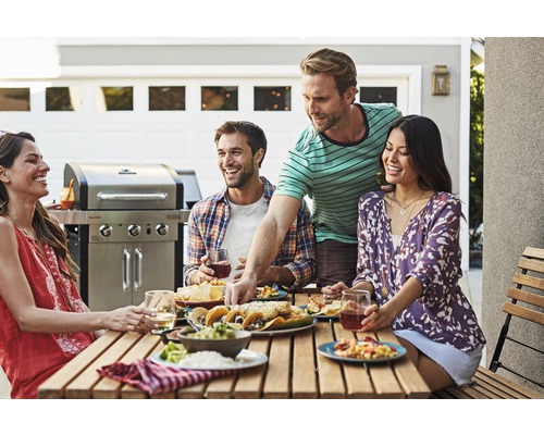 Groupe d''amis appréciant un repas en plein air avec un barbecue en arrière-plan.