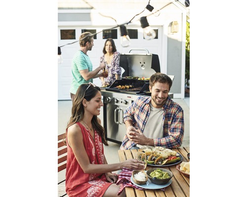 Un groupe de personnes fait des grillades et mange à l''extérieur, avec un barbecue, des tacos et du guacamole sur la table.
