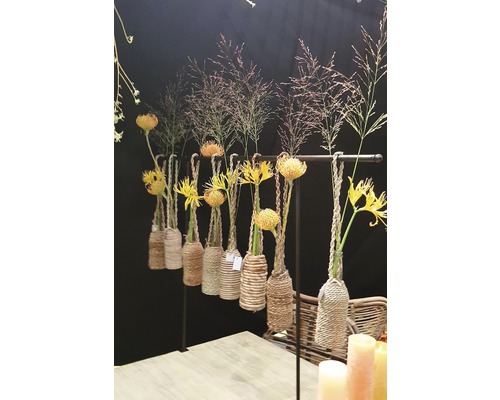 Arrangements floraux décoratifs dans des vases en corde, suspendus à une barre.