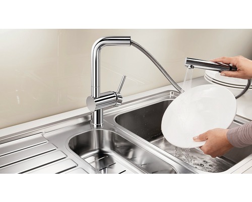 Edelstahlspüle mit verchromtem Wasserhahn und Geschirrbrause beim Abwaschen eines Tellers