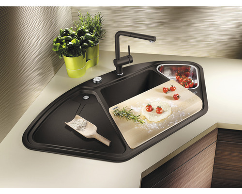 Eckspüle mit Armatur, Schneidebrett, Kräutern und Tomaten auf der Arbeitsfläche.