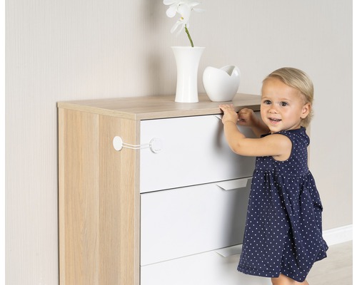 Kindersicherung an einer Kommode mit Schubladen befestigt, während ein Kind daneben steht.