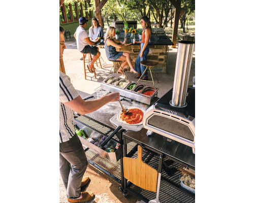 Szene mit Pizzaofen, Zutaten und Personen im Freien, die Pizza zubereiten