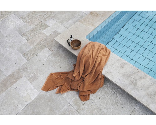 Vue sur une piscine avec serviette et produits de soin sur le sol en pierre