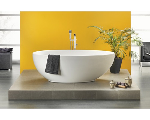 Freistehende Badewanne mit Armatur, Handtuch und Dekoration auf Podest vor gelber Wand