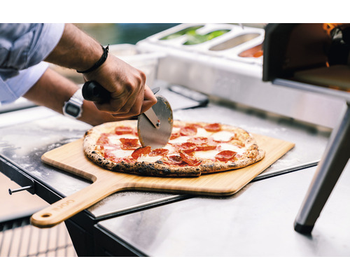 Eine Pizza wird auf einem Holzschieber mit einem Pizzaschneider geschnitten.