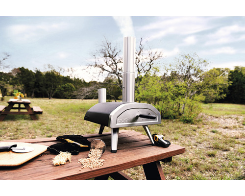 Four à pizza Ooni sur une table en bois à l''extérieur avec des accessoires de pizza.