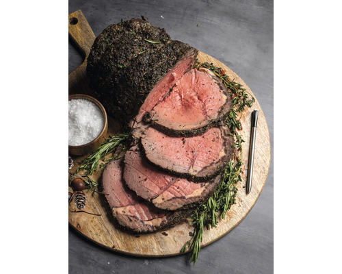 Rôti de bœuf aux herbes sur planche en bois avec sel et thermomètre.
