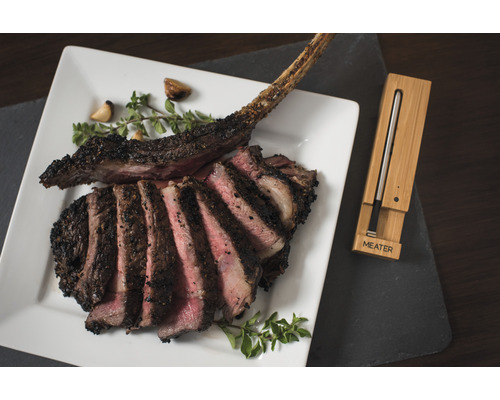 Steak Tomahawk sur une assiette avec des herbes et de l''ail, accompagné d''un thermomètre à viande