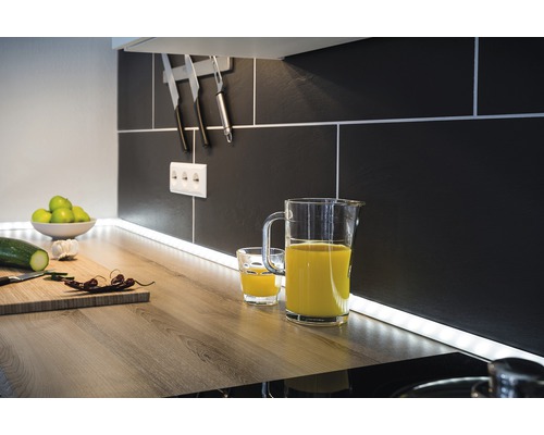 Scène de cuisine avec pichet de jus, verre, planche à découper et ustensiles de cuisine devant un dosseret de carreaux noirs