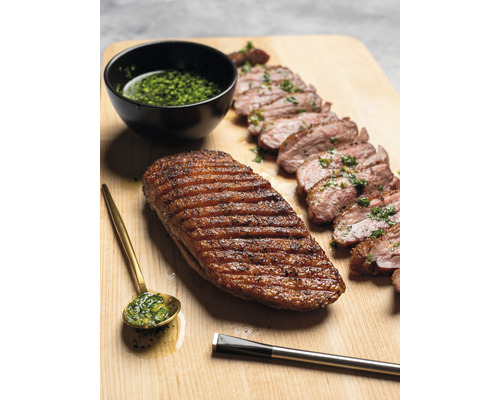Magret de canard grillé, tranché, avec sauce aux herbes, cuillère et pinceau sur planche en bois