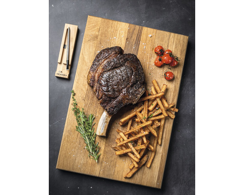 Steak Tomahawk avec frites, tomates et herbes sur une planche à découper
