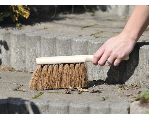 Hand fegt mit einer Kehrbürste eine Steintreppe