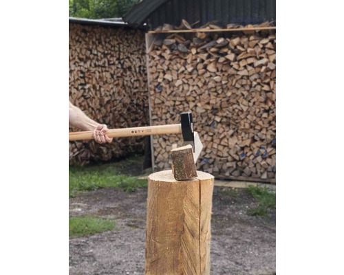 Couper du bois avec une hache sur un billot devant une pile de bois