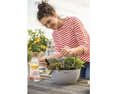 Femme plantant des herbes aromatiques dans un bac à fleurs sur une table en bois