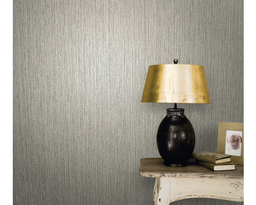 Gros plan d''un mur avec un papier peint à effet de structure verticale à côté d''une table avec une lampe, des livres et un cadre photo.