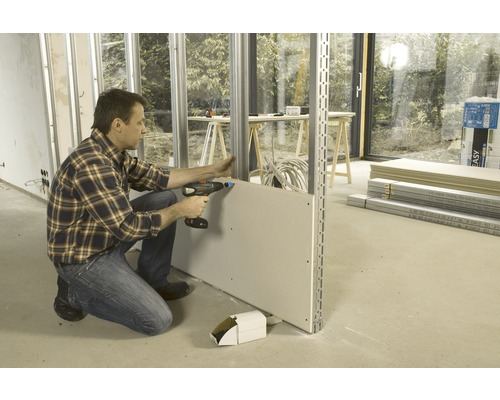 Mann montiert eine Gipskartonplatte an einer Metallunterkonstruktion mit einem Akkubohrschrauber.