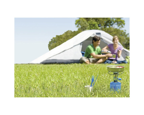 Szene mit Gaskocher, Campinggeschirr und Zelt im Freien auf einer Wiese.