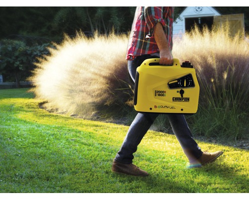 Un homme transporte un générateur Champion jaune dans le jardin.