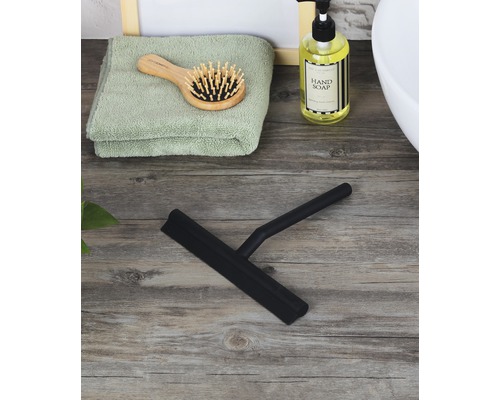 Raclette de douche noire sur une table en bois avec serviette, brosse à cheveux et savon