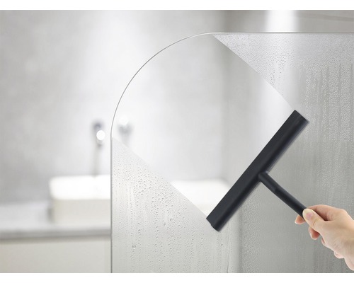 Une main essuie une paroi de douche avec une raclette