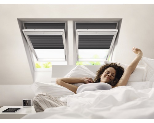 Femme allongée dans un lit sous des fenêtres de toit avec des stores