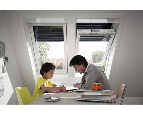Père et fils sont assis à table sous des fenêtres de toit en train de peindre.