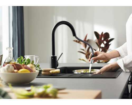 Une personne rince des légumes dans un évier avec un robinet de cuisine noir.