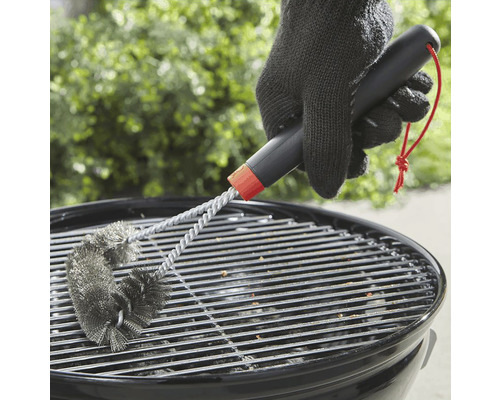 Une personne nettoie une grille de barbecue avec une brosse à barbecue.