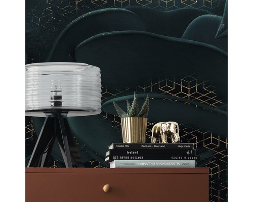 Scène décorative avec lampe, plante, figurine décorative et livres sur une commode devant un papier peint à motifs