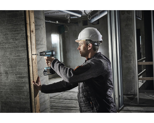 Un homme portant un casque de protection perce un trou dans une planche de bois avec une perceuse sans fil sur un chantier.