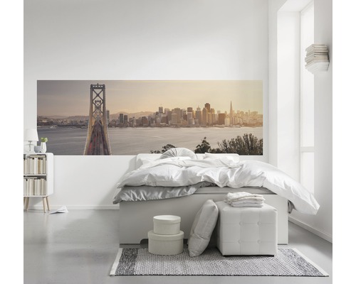 Chambre lumineuse avec une fresque murale représentant un paysage urbain, un lit et une table de chevet