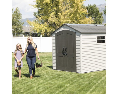 Scène de jardin avec une cabane de rangement avec porte double et fenêtre, et une femme et une fille portant des paniers sur la pelouse