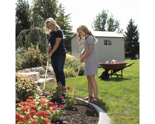 Une femme et une fille désherbent un parterre de fleurs dans le jardin avec des râteaux de jardin.