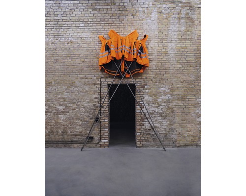 Plusieurs gilets de sécurité sur un support métallique devant un mur de briques