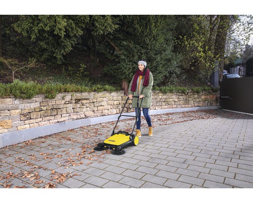 Femme utilisant une balayeuse jaune pour enlever les feuilles mortes d''une allée.