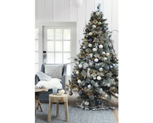 Sapin de Noël décoré avec des lumières, des boules de Noël et des décorations rustiques dans un salon.