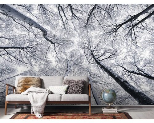 Papier peint photo avec motif de forêt hivernale dans un salon avec canapé et décorations.