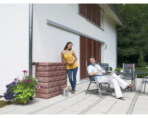 Scène avec réservoir d''eau de pluie aspect pierre, fleurs, couple sur la terrasse et façade de maison