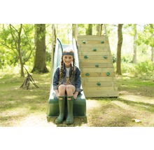 Mädchen sitzt auf einer Rutsche mit Kletterwand im Garten.