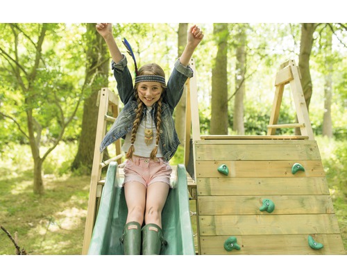 Mädchen mit Indianerkopfschmuck auf einem Spielturm mit Rutsche und Kletterwand im Garten