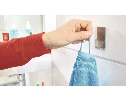 Une main suspend une serviette bleue à un crochet pour serviette dans la salle de bain