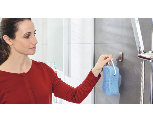 Frau hängt Badeschwamm an einen Haken in einer Dusche