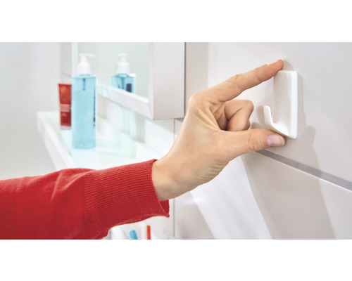 Main fixant un crochet autocollant sur un mur de salle de bain