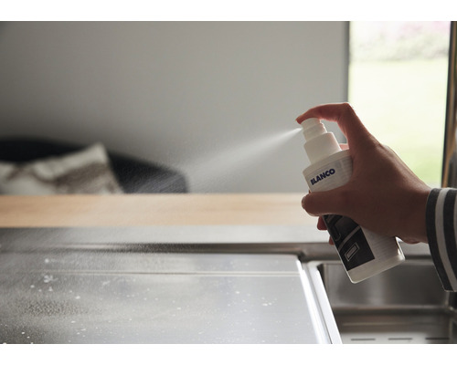 Une main vaporise du nettoyant d''un vaporisateur Blanco sur un évier en acier inoxydable.