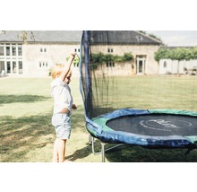 Un enfant se tient à côté d''un trampoline dans le jardin.