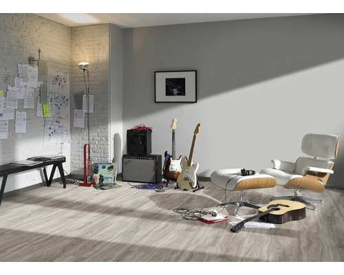 Pièce lumineuse avec sol stratifié, guitares, amplificateurs et fauteuil.